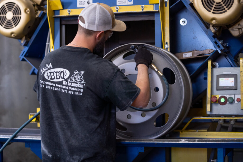 Technician grinding a metal wheel rim before powder coating at Biltwood Powder Coating.