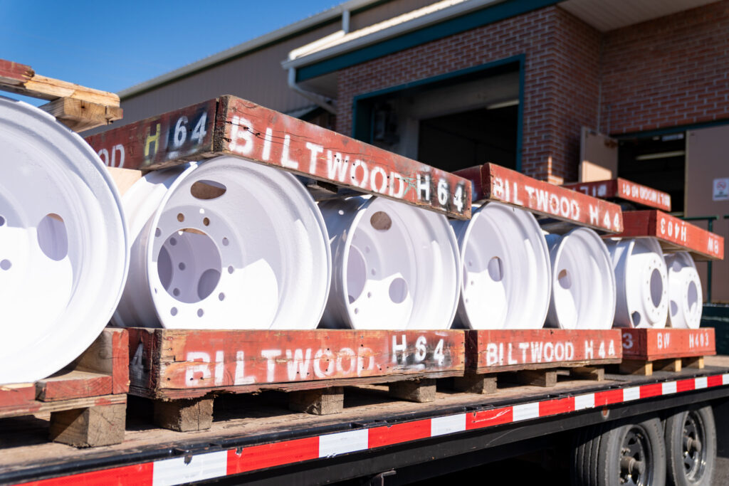 Freshly powder-coated white industrial wheel rims stacked in custom Biltwood Powder Coating crates.